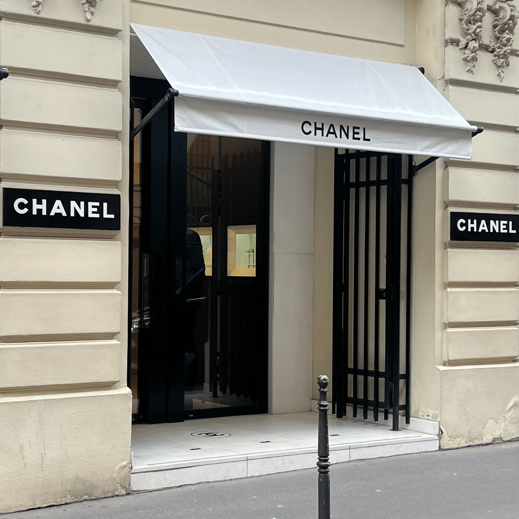 Chanel store entrance with white awnings and brand name signs.