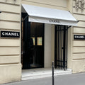 Chanel store entrance with white awnings and brand name signs.